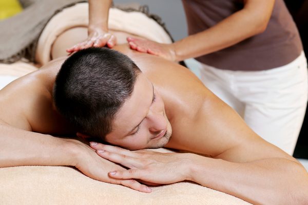 Handsome man is lying on the couch while being massaged at a spa salon